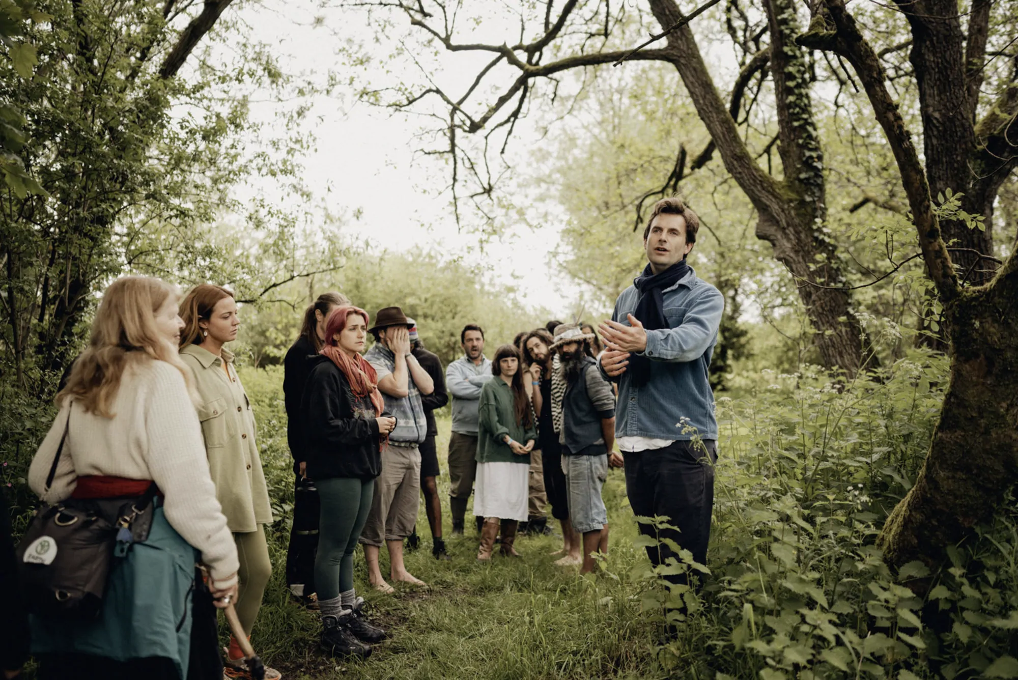 A group gathered under the trees, listening to a facilitator
